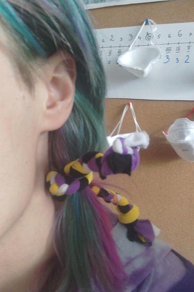 close selfie with view on hair ribbon in nonbinary flag color. behind person, there are FFP3 masks hanged on room wall
