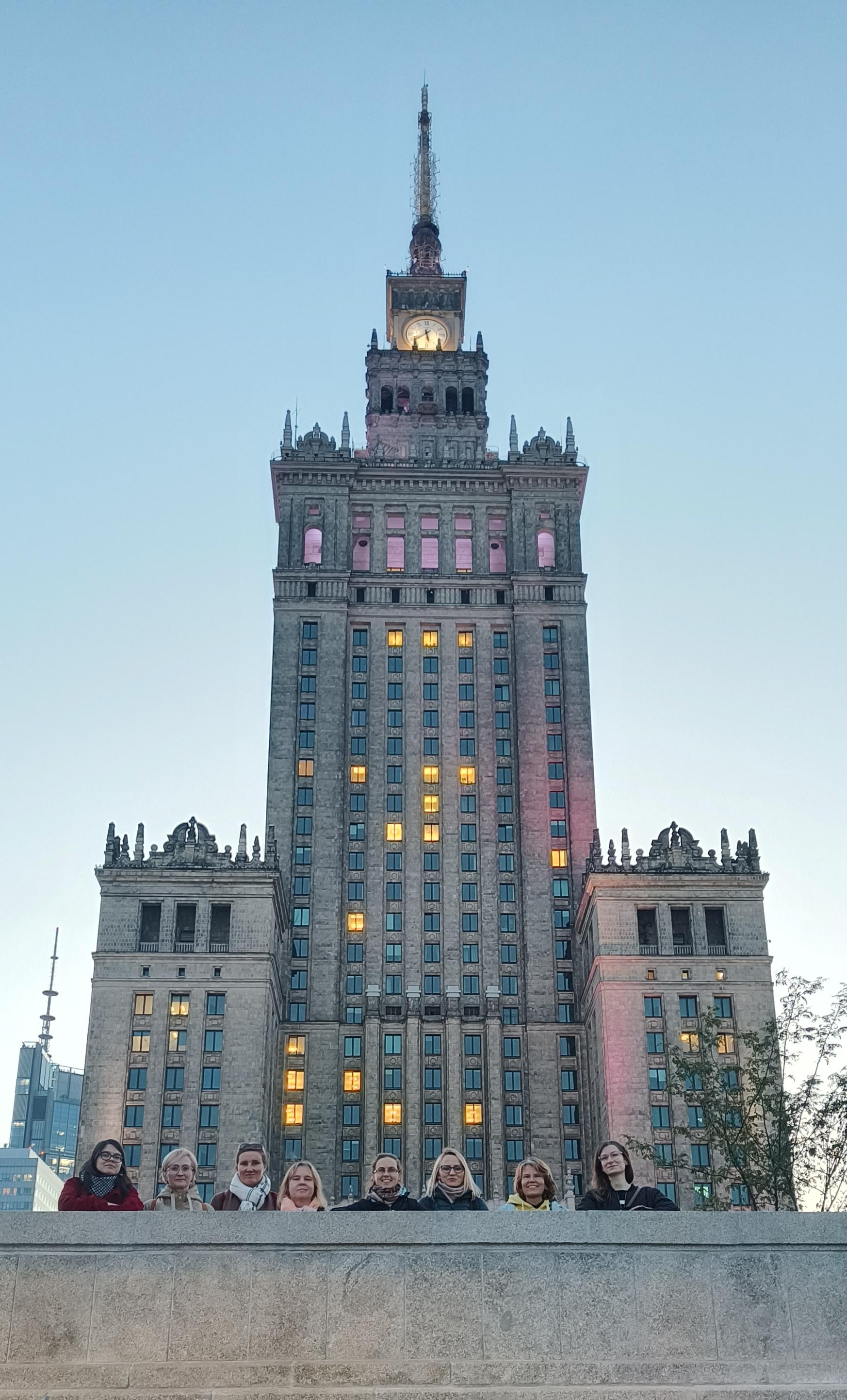 Zdjęcie Pałacu Kultury i Nauki w Warszawie, przed nim osiem pracowniczek i współpracowniczek Watchdog Polska.