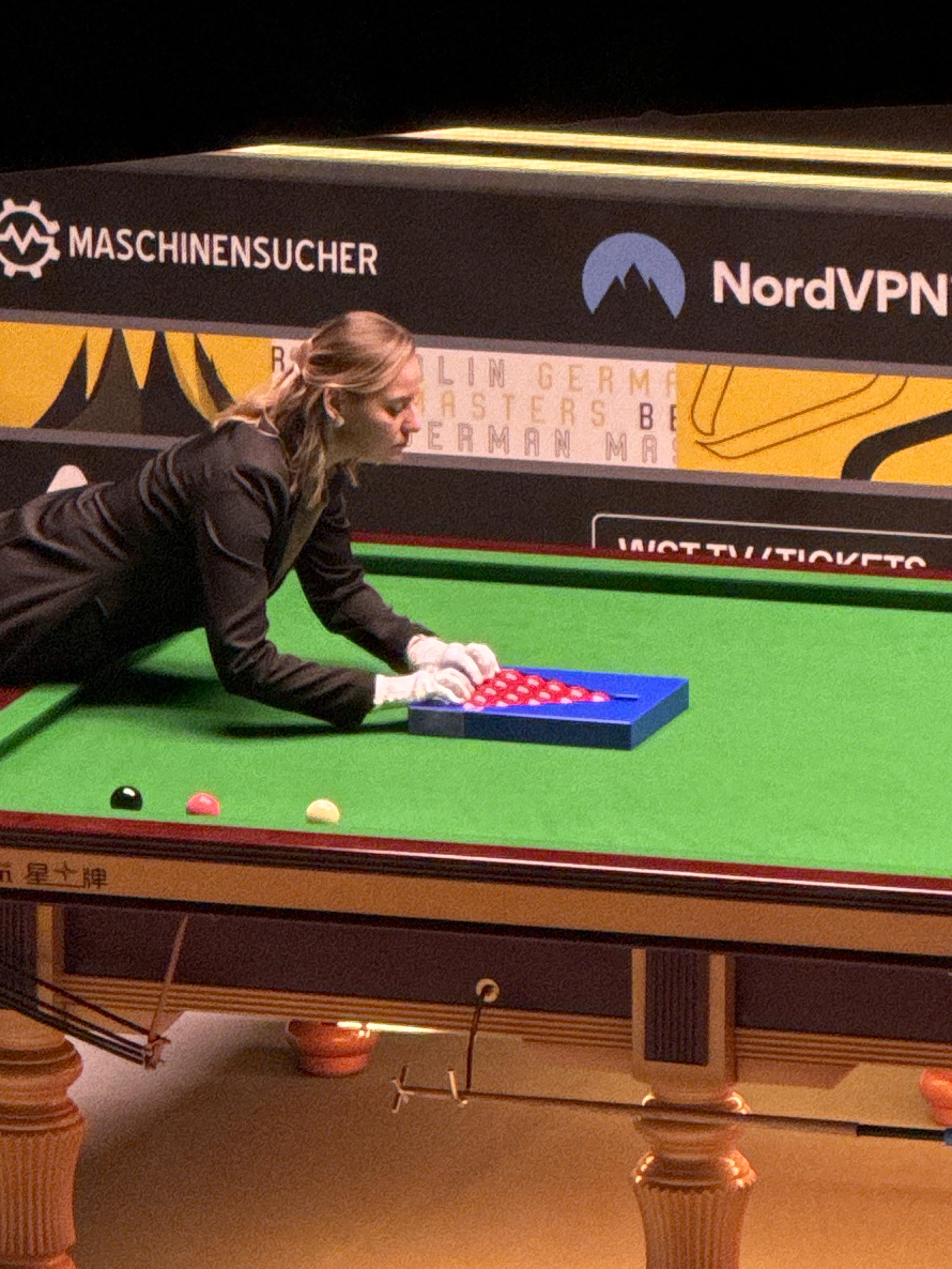 Mecz snookera, ćwierćfinał German Masters. Sędzina ustawia przy pomocy narzędzia trójkąt złożony z 15 czerwonych bil.