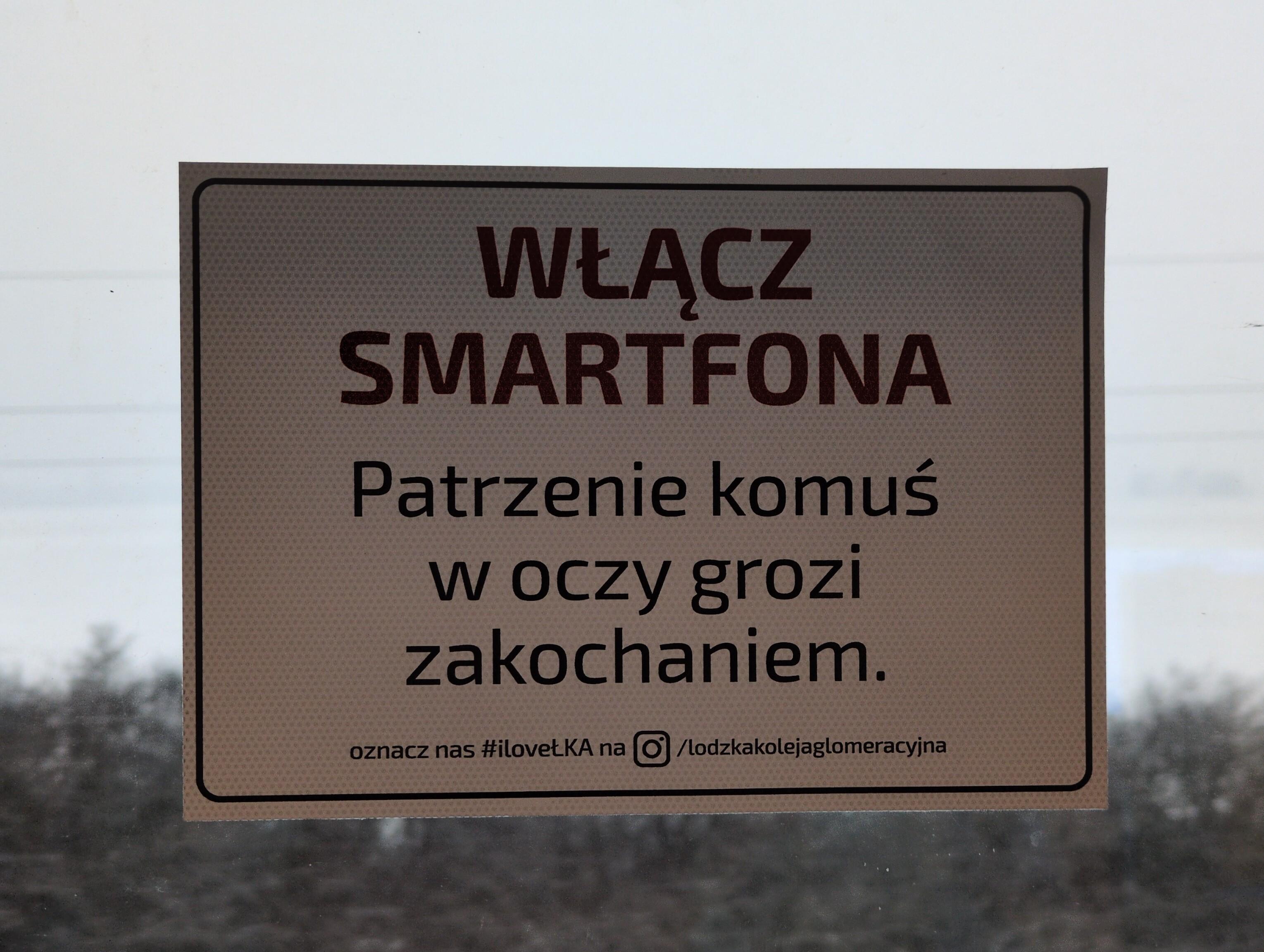 Nalepka na oknie. Wielkimi literami "włącz smartfona". Poniżej "Patrzenie komuś w oczy grozi zakochaniem." Na dole odniesienie do Instagrama.