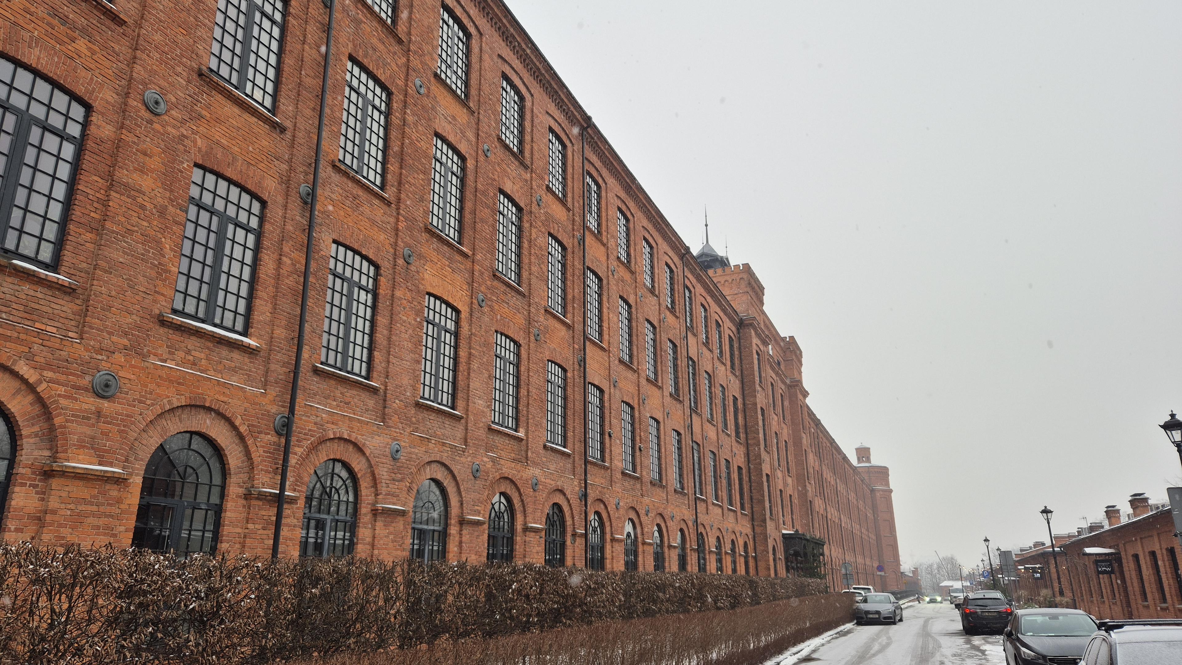 Długi, trzypiętrowy budynek pofabryczny z czerwonej cegły, odrestaurowany na mieszkania. Ciągnie się na kilkaset metrów od lewej strony kadru do centralnej części.