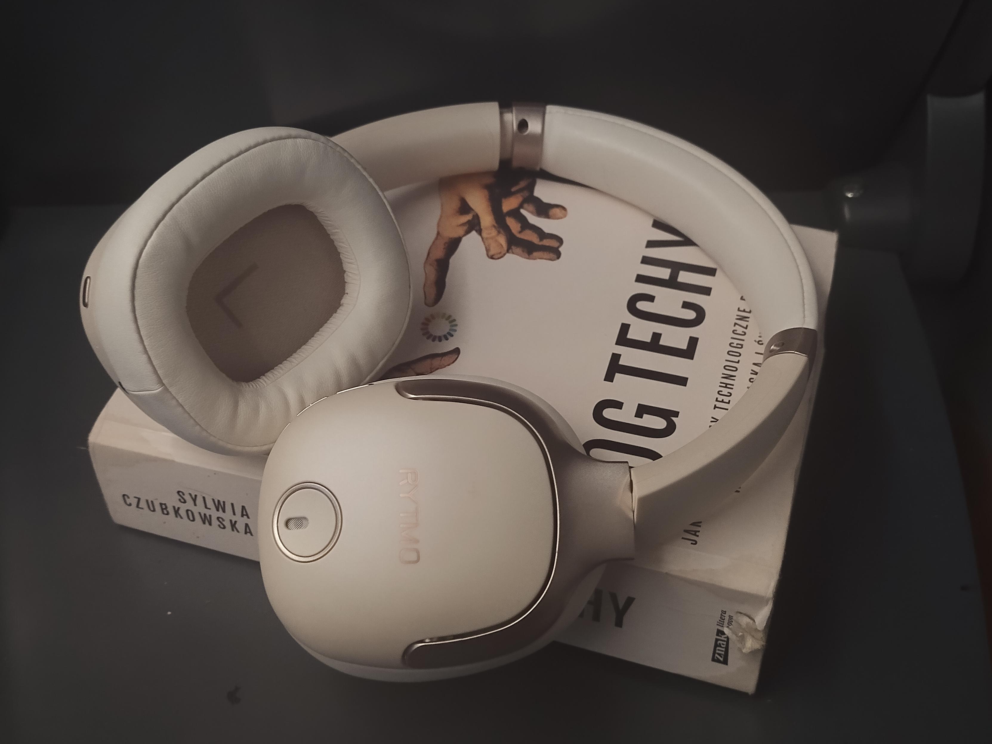 Słuchawki nauszne w kolorze perłowym leżące na książce "Bóg Techy"