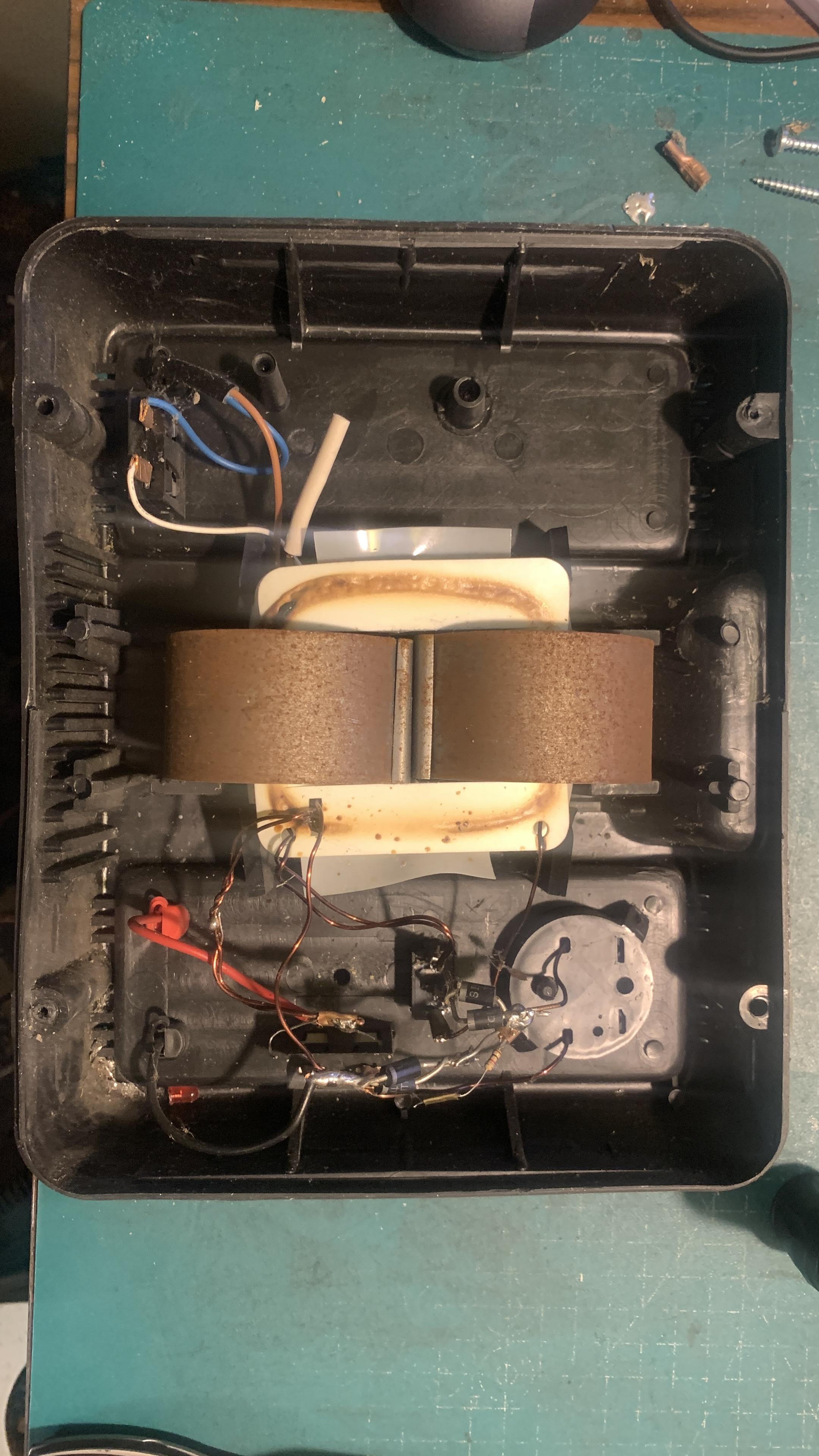 Wnętrzne popsutego prostownika, kable i diody w chaosie, przegrzany transformator z dwoma uzwojeniami.