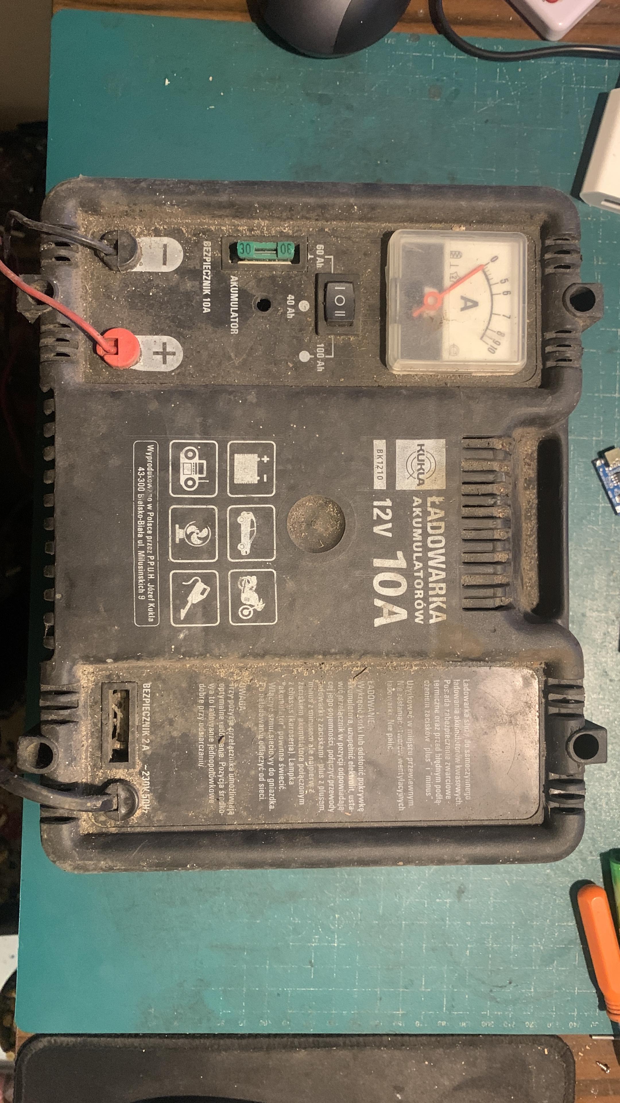 Przód obudowy prostownika. Brudny. Widać amperomierz, kabelki i bezpieczniki oraz opisy.