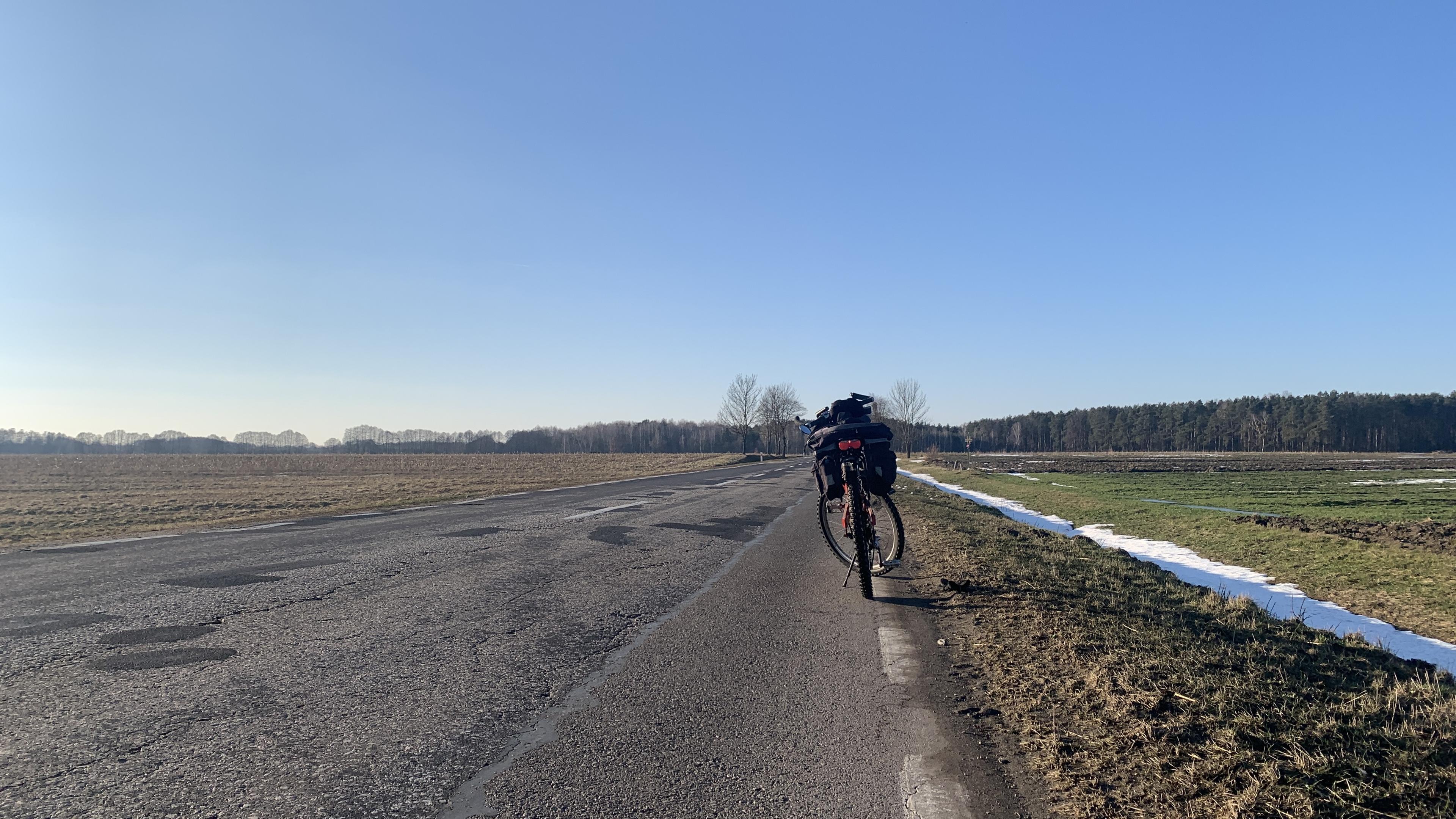 Rower na drodze gminnej, obok pola i las w tle. Ładne niebo. Roztopy