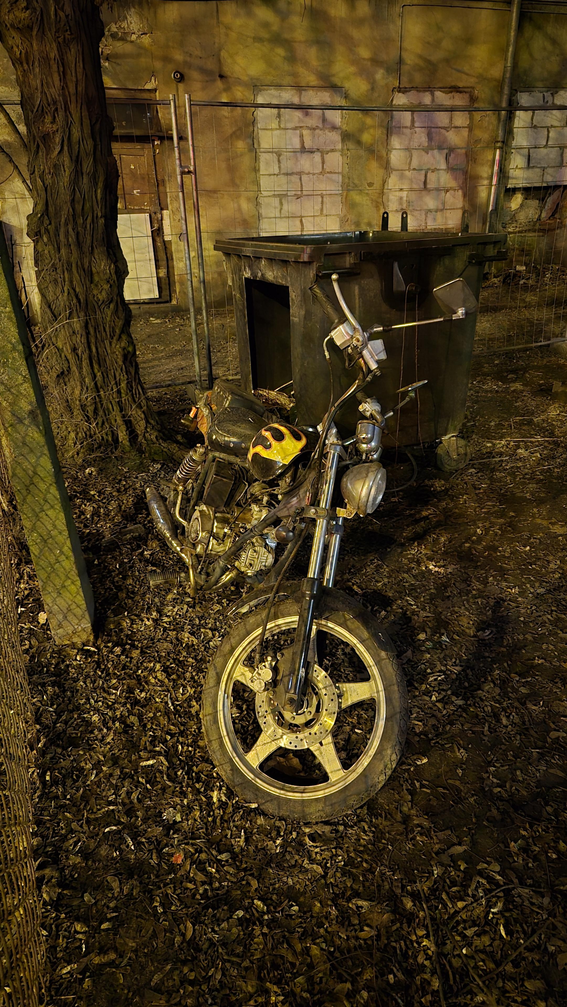 Ten sam skuter, na tle opuszczonej komórki i puszki na śmieci.