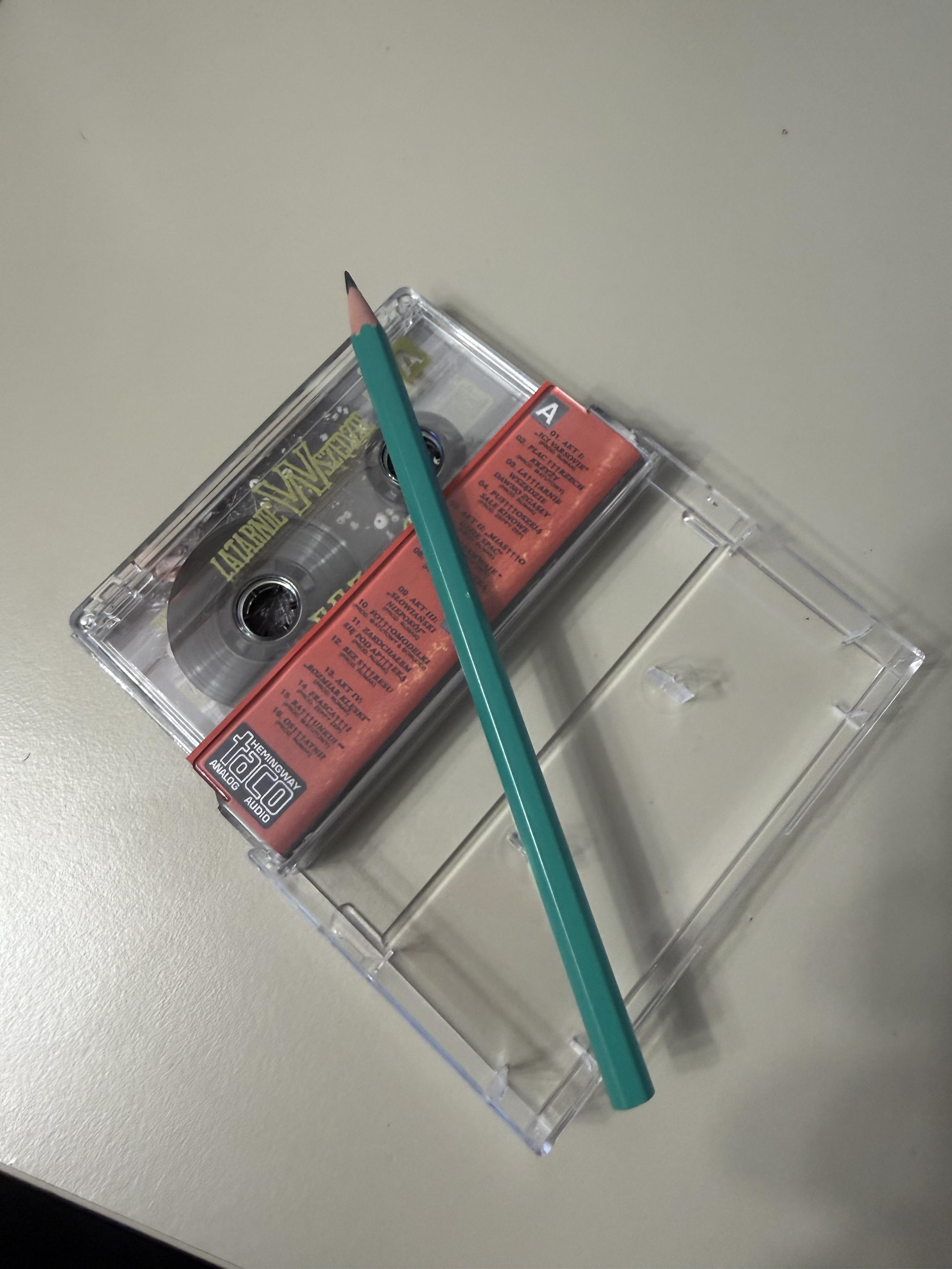 Ołówek położony na otworzonym opakowaniu z kasetą magnetofonową dodawaną do preorderu najnowszego albumu Taco Hemingwaya "Latarnie Wszędzie Dawno Zgasły"