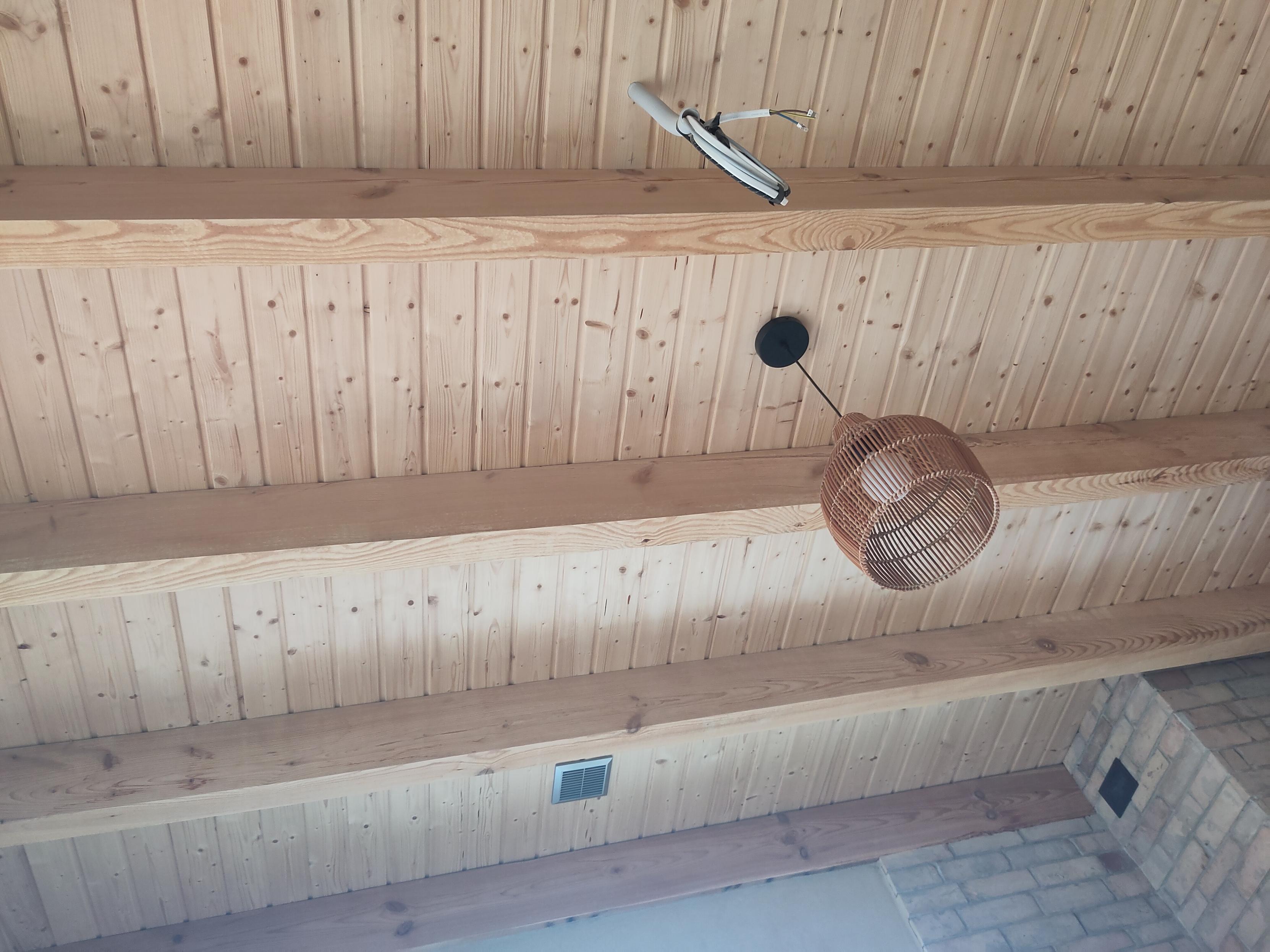 Zdjęcie drewnianego sufitu z widocznymi belkami. Z sufitu zwisa lampa i pęk kabli