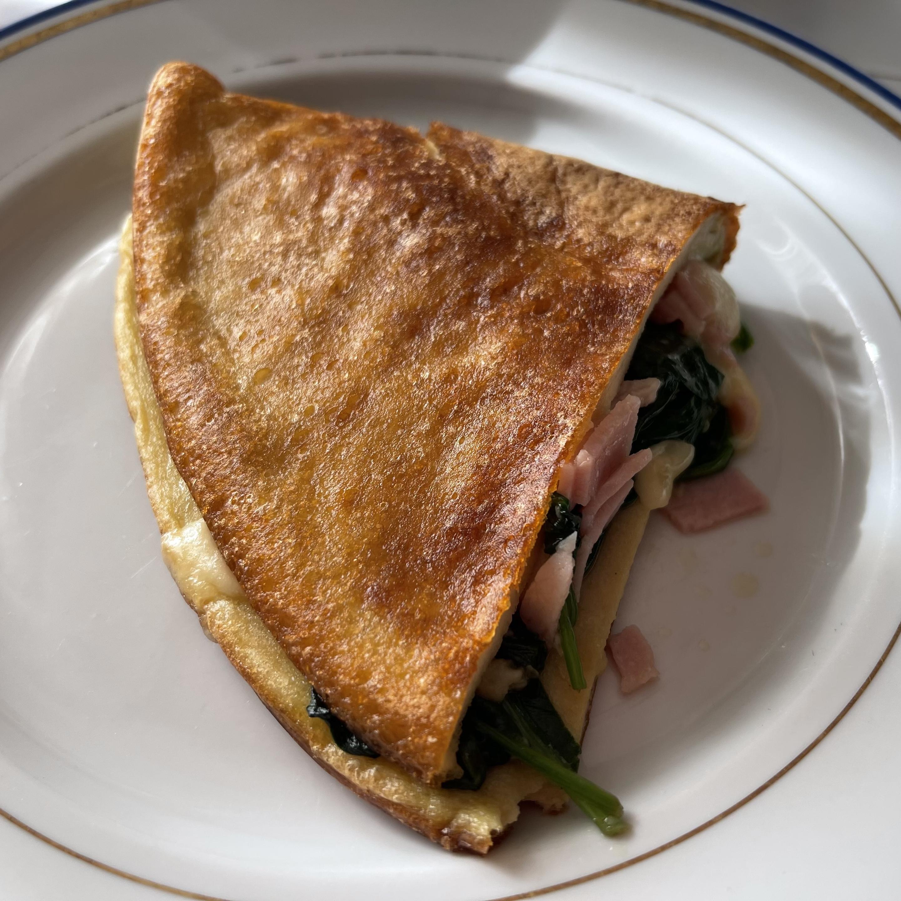 Na białym talerzu leży złożony na pół, złocisto zrumieniony omlet. Z wnętrza wystaje farsz ze szpinaku, kawałków szynki oraz roztopionego wędzonego sera.