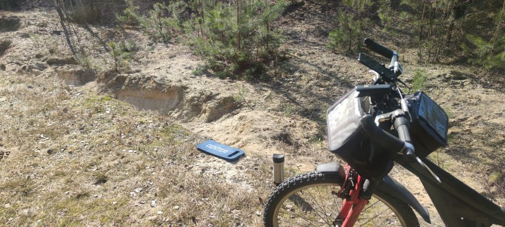 Rower, podkolannik i kubek termiczny z kawą w lesie, w miejscu wydobywania piasku