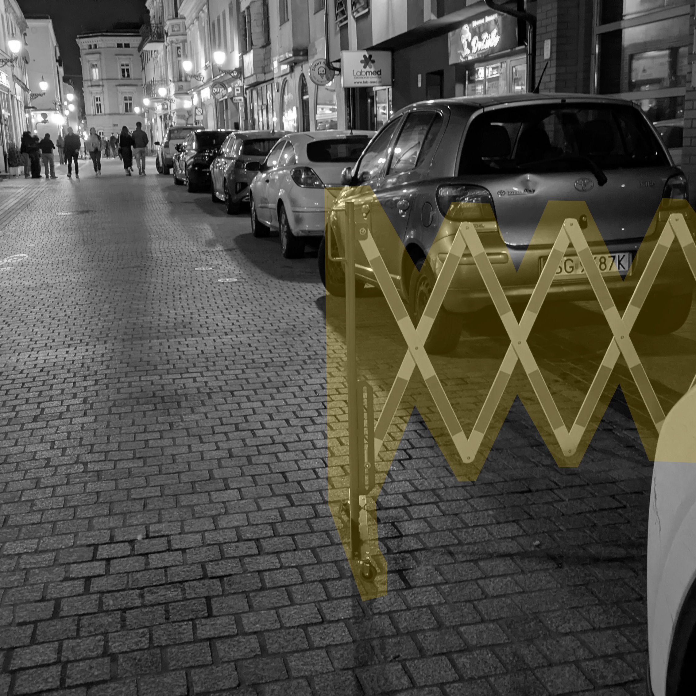 harmonijkowa, składana barierka szeroka na około dwa metry, która ma blokować nieprawidłowe parkowanie. Za barierką zaparkowany sznur samochodów, które zignorowały zaporę.