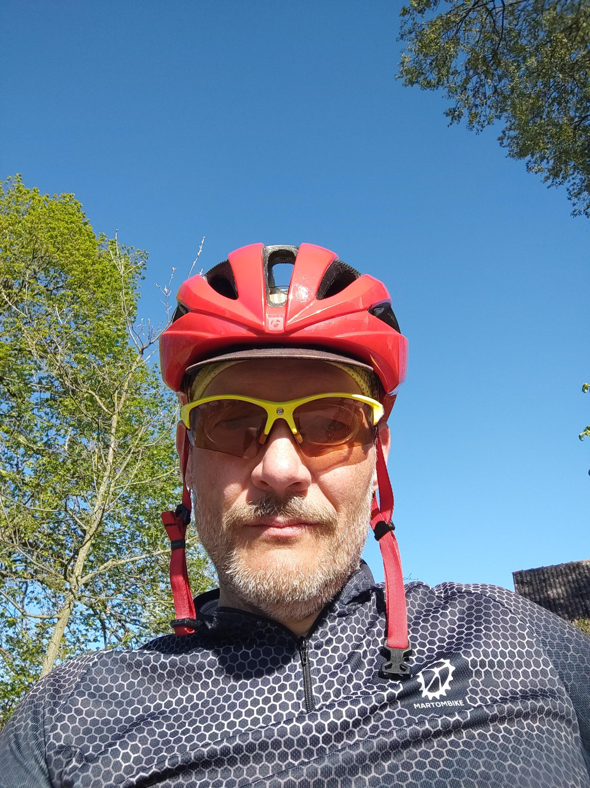 Selfie w czarnej koszulce rowerowej, żółtych okularach i czerwonym kasku.