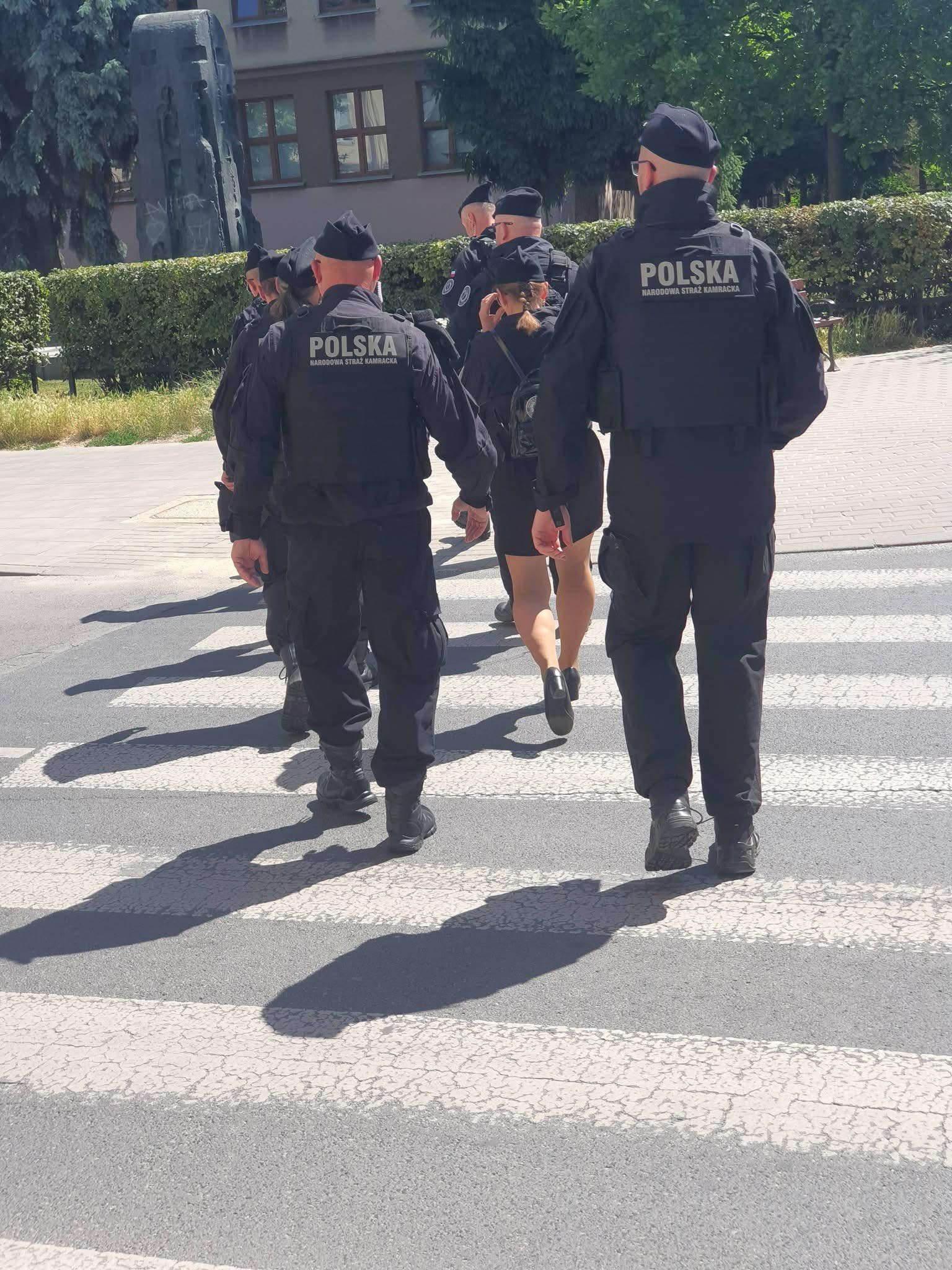 Osoby w czarnych mundurkach i furażerkach udających policyjne, z napisem Polska zamiast Policja