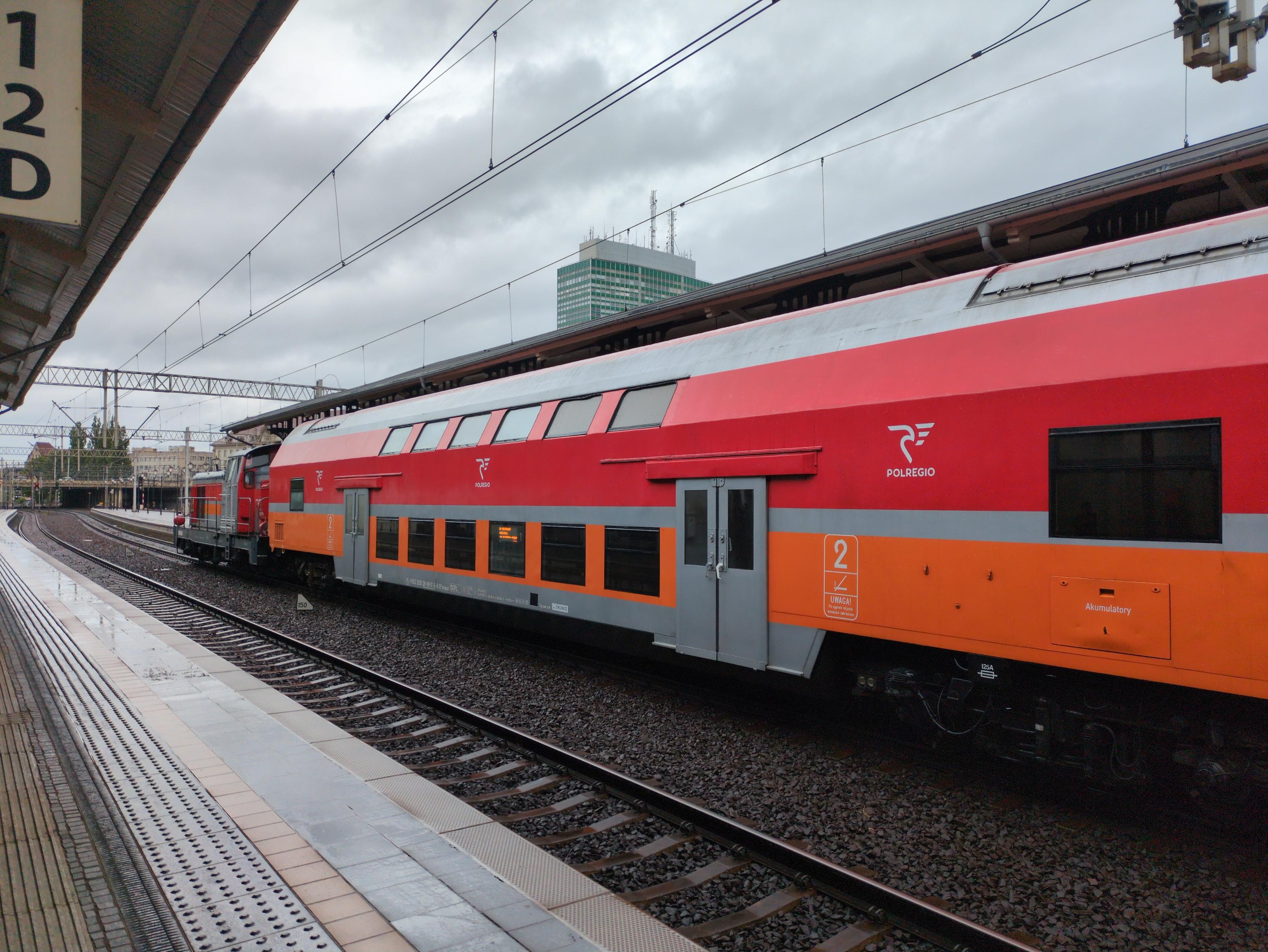 Pociąg w pomarańczowo-czerwono-szarych barwach PolRegio. Z przodu lokomotywa typu stonka (SM42), a za nią piętrowy wagon typy bohun. Pośrodku widać dwa rzędy okien: na dole i z ukosa na górze. Dalej dwuskrzydłowe rozsuwane drzwi i pojedyncze, szerokie okno na półpiętrze, po obydwu końcach wagonu. W ramach nowoczesnego akcentu, wyświetlacz punktowy w oknie.