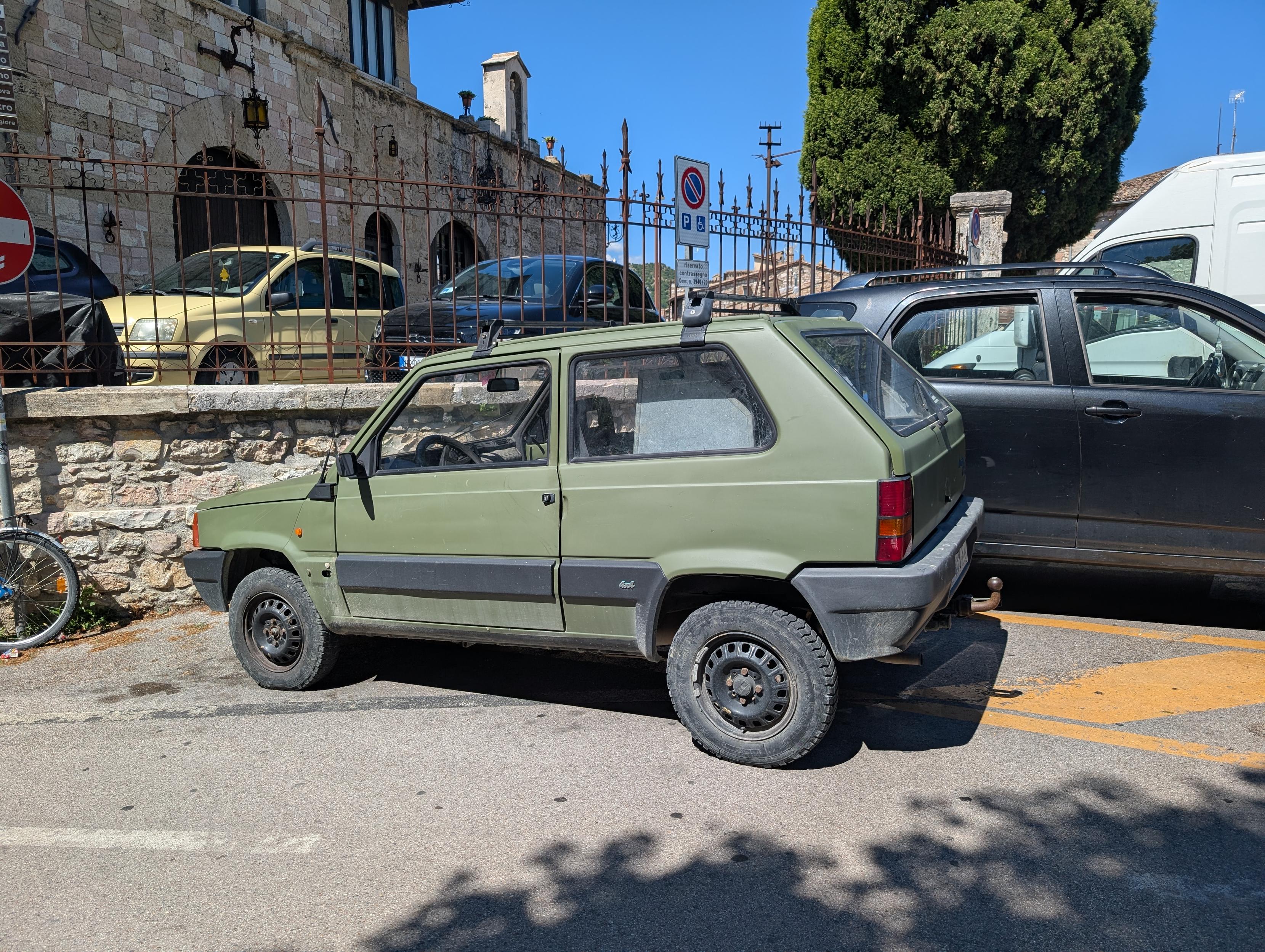 Fiat panda 4x4 pierwszej generacji, kolor khaki, na parkingu współczesnego średniowiecznego miasteczka we Włoszech.
