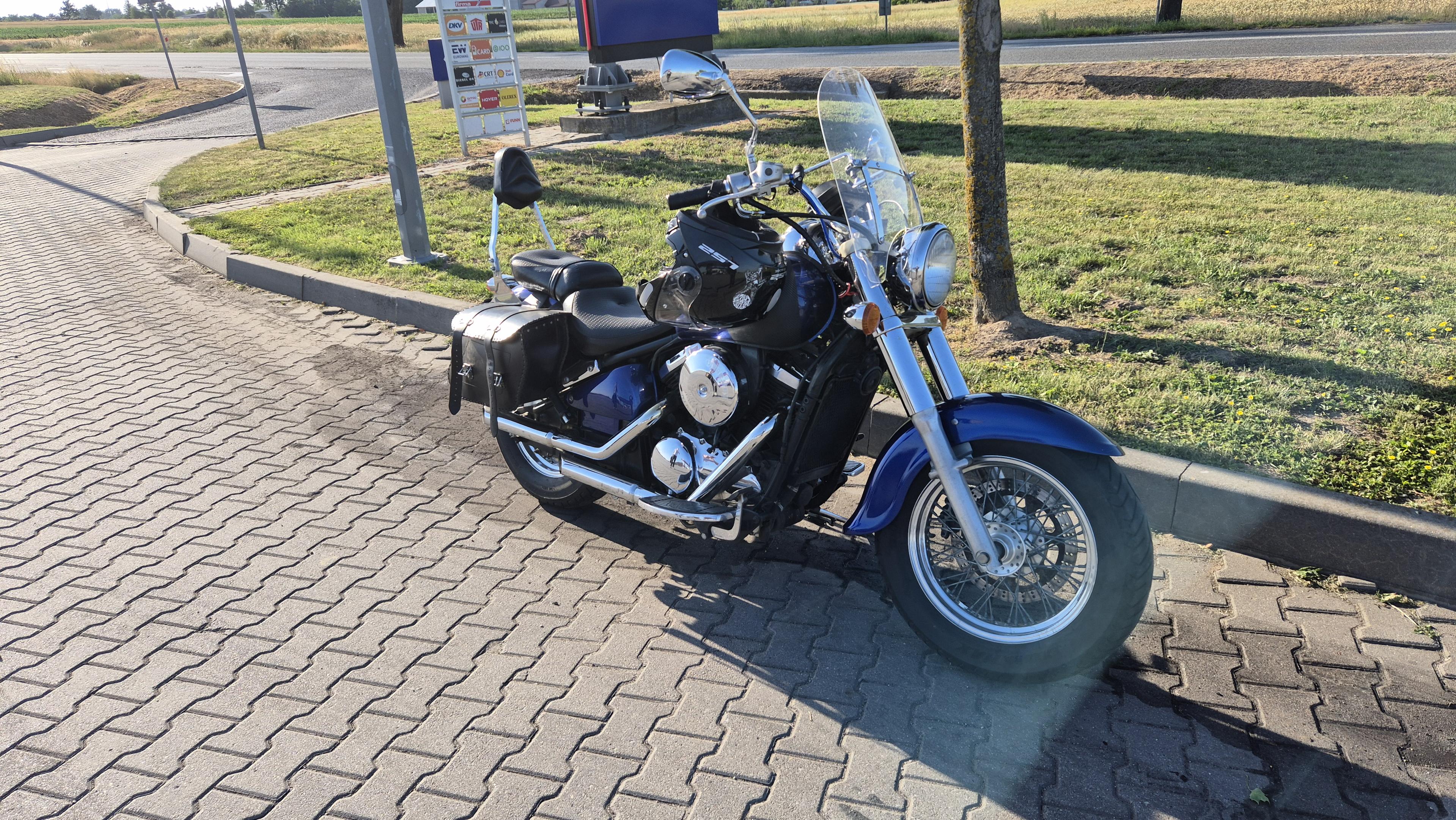 Motocykl, duży niebieski cruiser z sakwami, zaparkowany na poboczu drogi, podczas przejazdu gdzieś w trasie.