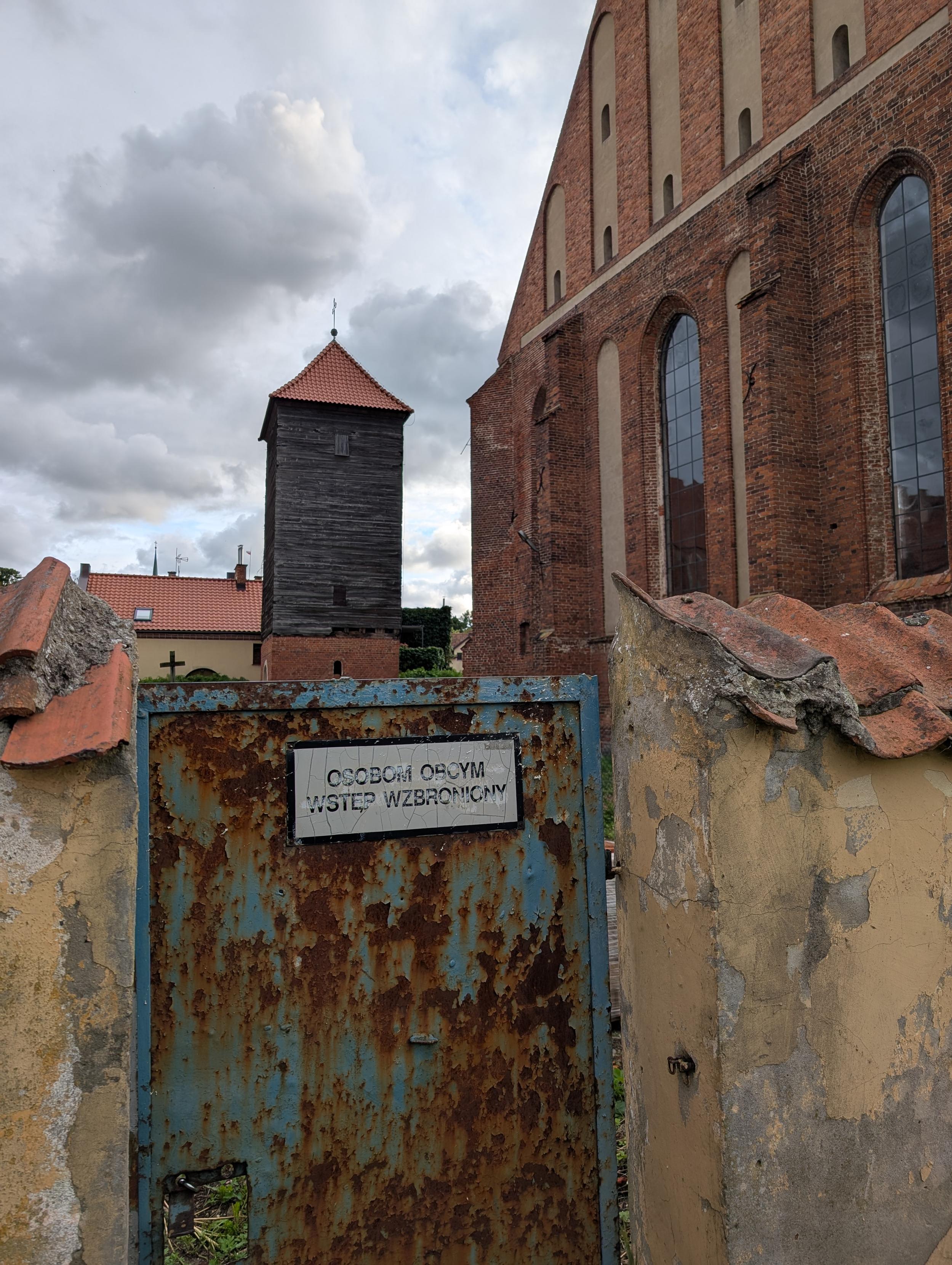 Zniszczony stary kościół, mur, na pordzewiałej furtce napis "obcym wstęp wzboroniony"