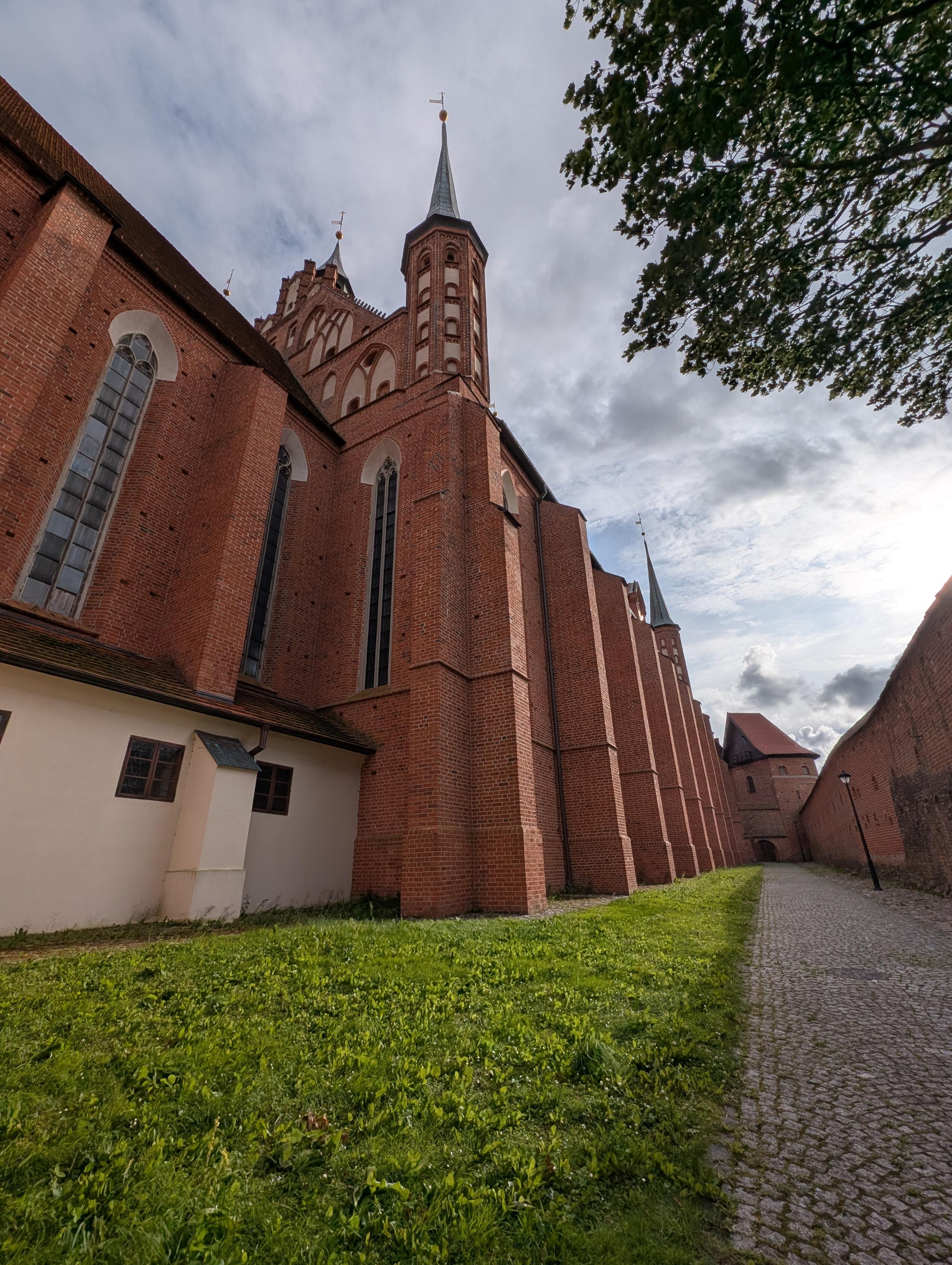 Bok katedry, ujęcie z dołu, wysokie mury z czerwonej cegły, pas trawy, kamienna ścieżka