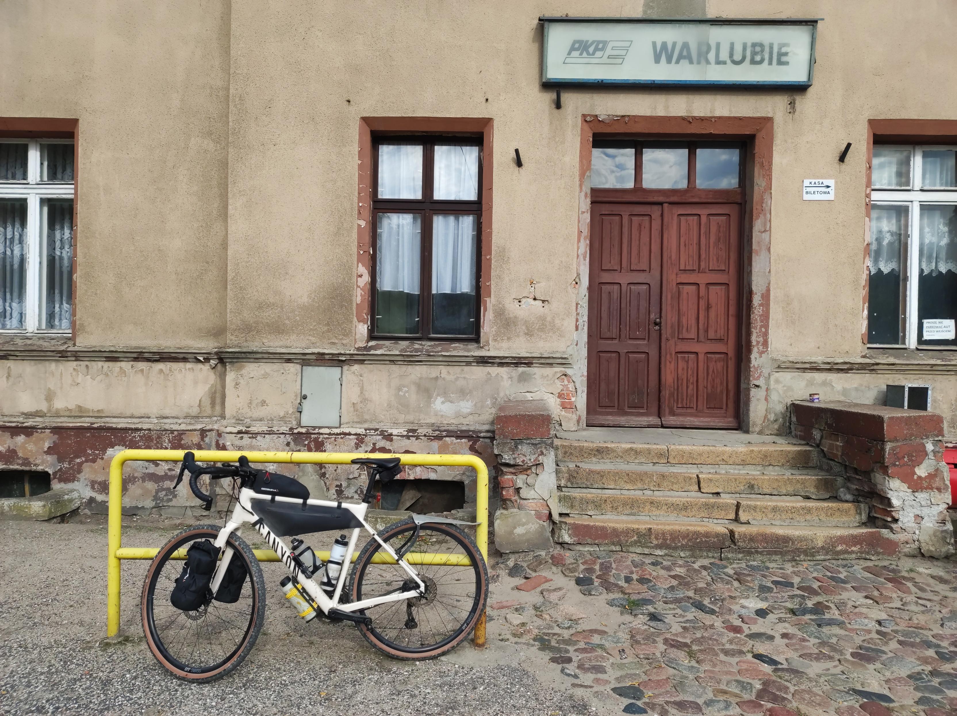 Przed wejściem do podniszczonego budynku dworca kolejowego Warlubie jest żółta barierka, o którą koperta się mój rower.
