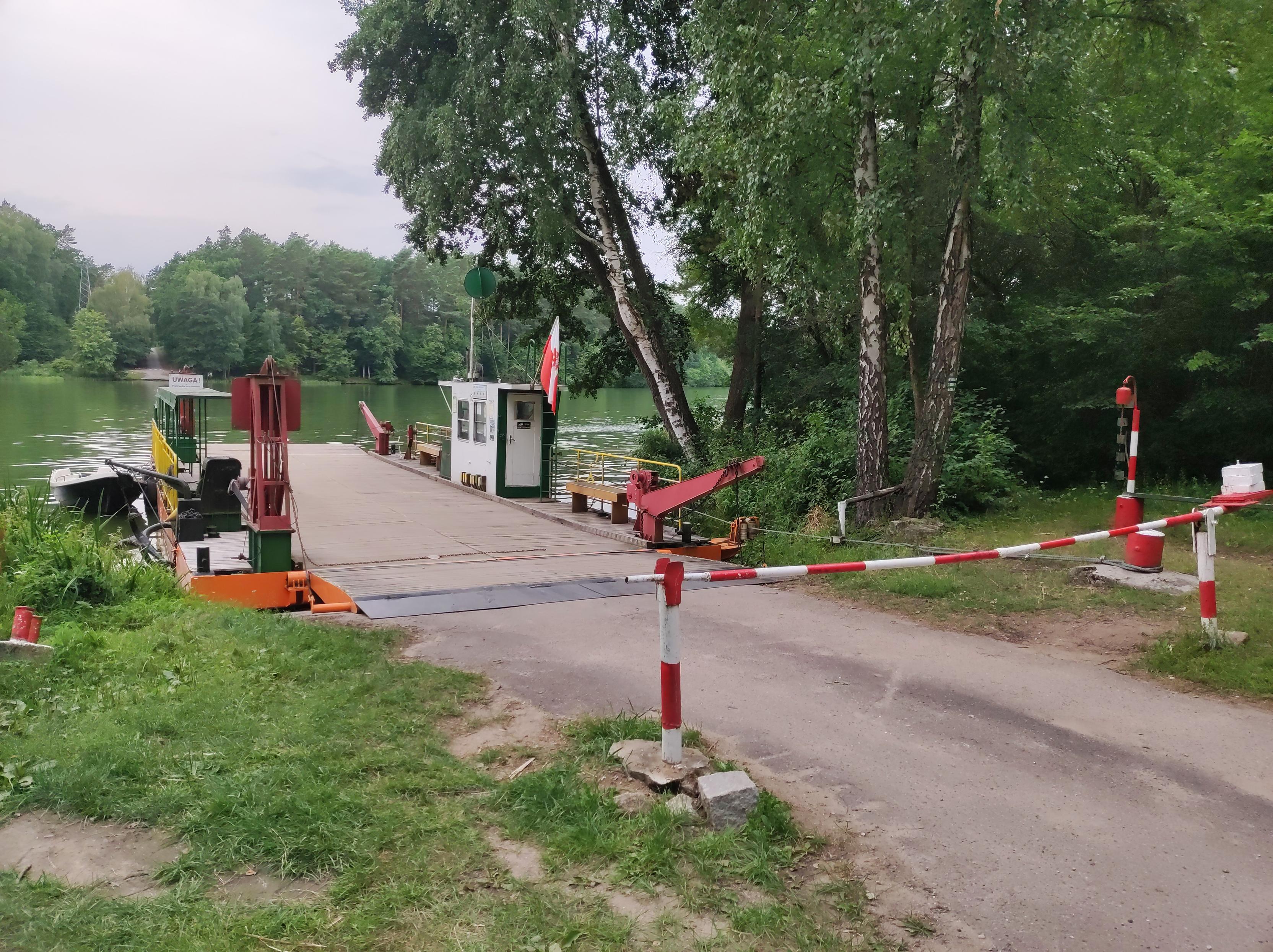 Prom na zalewie przycumowany do brzegu za opuszczonym szlabanem.