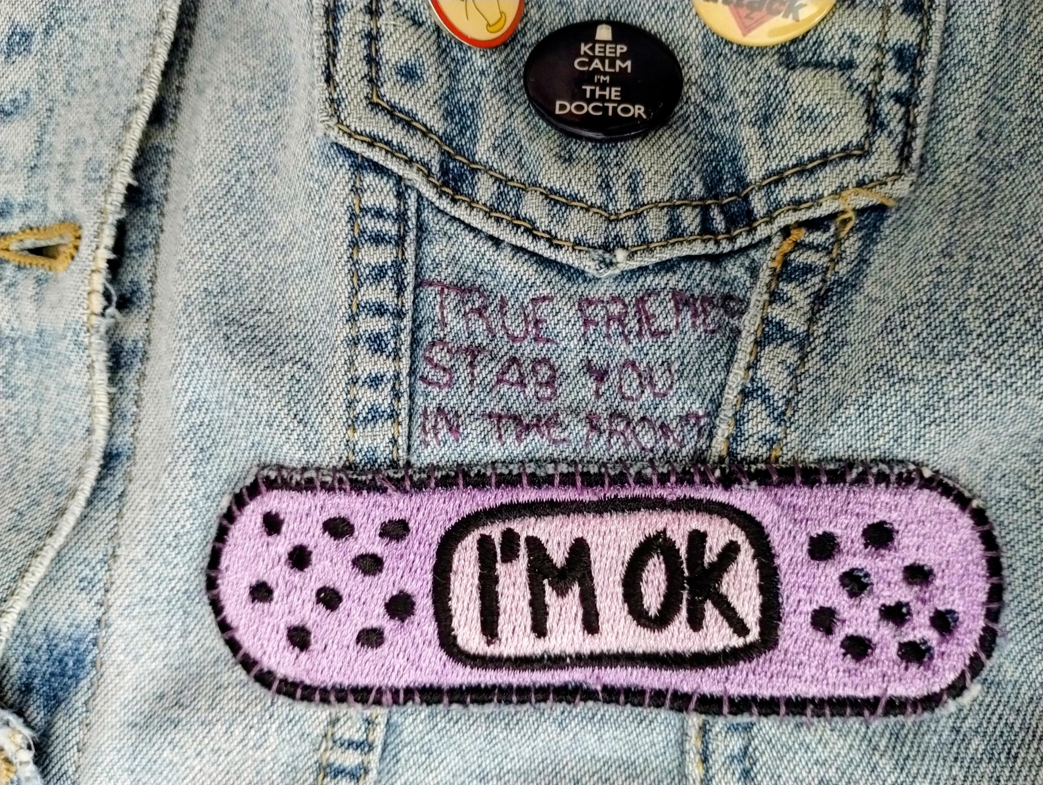 Nad naszywką w kształcie plasterka z napisem I'M OK wyhaftowany na materiale kurtki napis "true friends stab you in the front" (cytat z Bring Me The Horizon). Mnie śmieszy, wybaczcie.