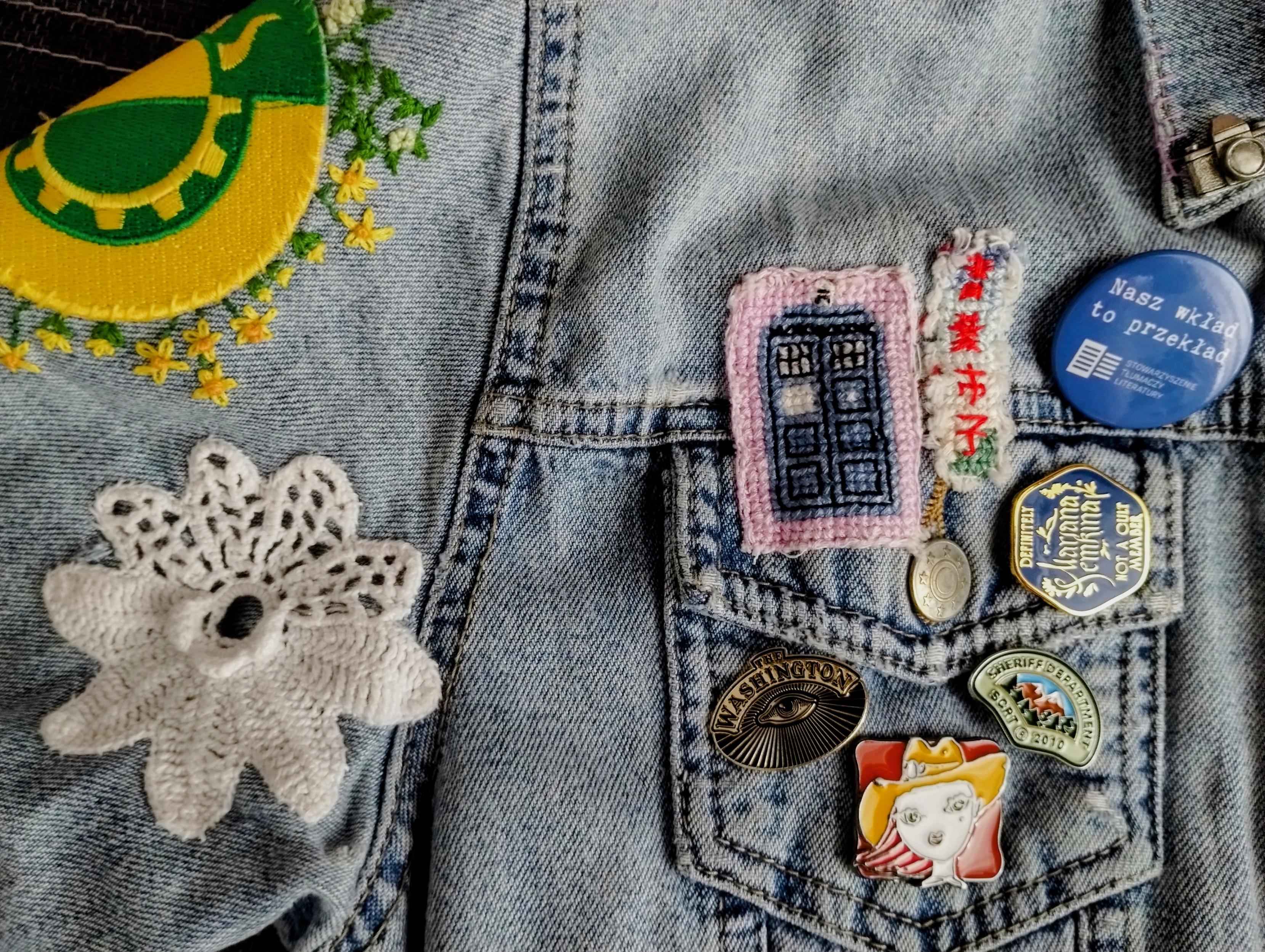 Zbliżenie na lewy rękaw i okolice kieszeni na piersi, widać dokładnie szydełkowany kwiatek mamy, naszywkę Tardis i przypinki.